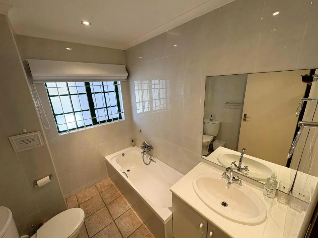 Bathroom with a built-in bathtub, twin vanity, and a large mirrored wall
