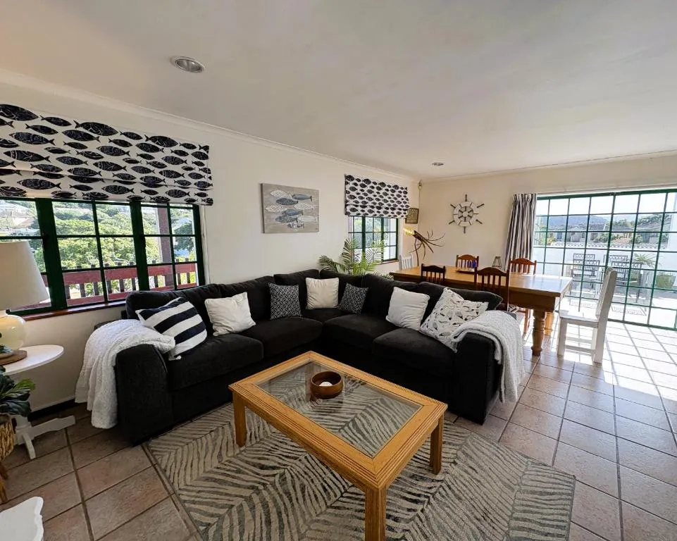 Open-plan lounge with a black corner sofa, fish-print blinds, and a dining table beyond