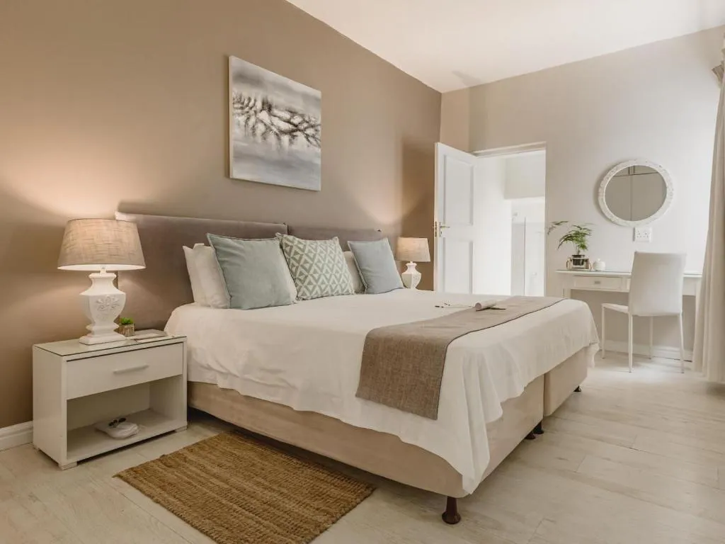 King bedroom in warm taupe tones with a tufted headboard, bedside lamps, and a dressing table