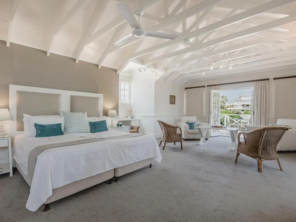 Vaulted-ceiling suite with a king bed, rattan lounge chairs, and French doors onto a balcony