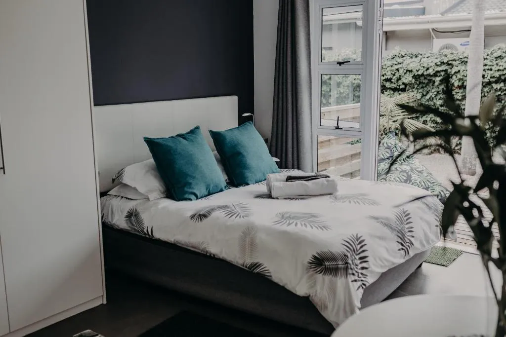 Bedroom with teal cushions and a botanical-print duvet opening onto a private patio