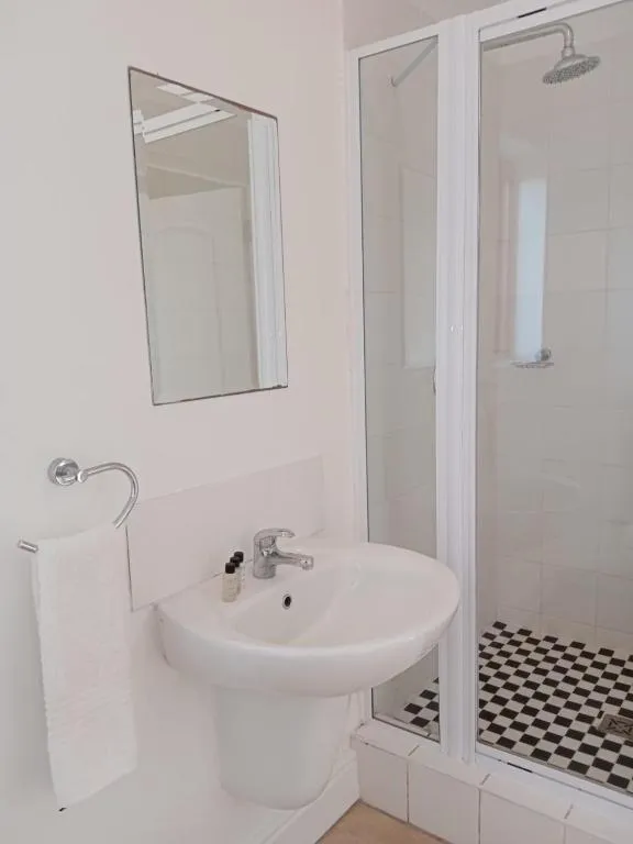 Bathroom with a pedestal basin, framed mirror and a glass-screened shower with chequered floor tile