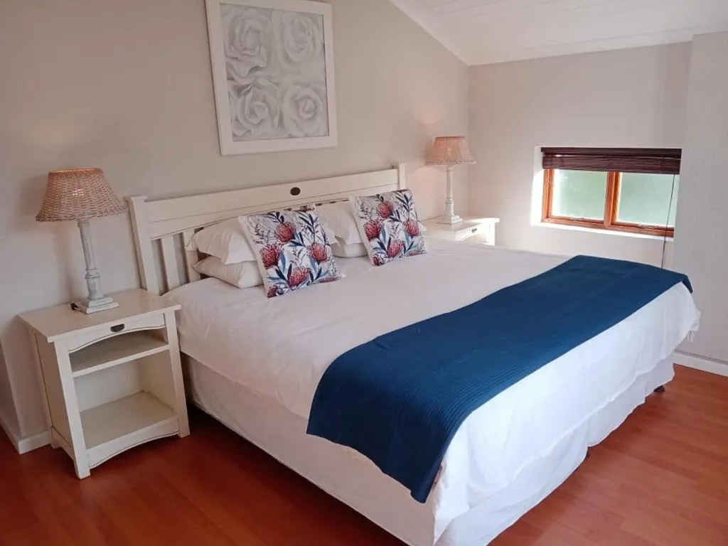 Bedroom with a white panelled headboard, Protea-print cushions and dark wood flooring
