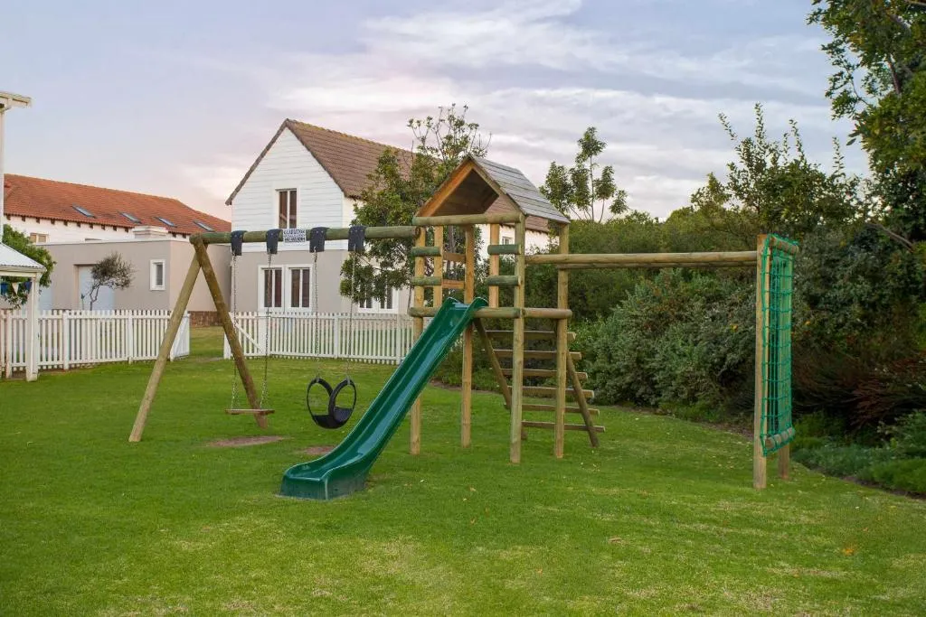 Shared children's play area with a slide, swings and climbing frame behind a picket fence