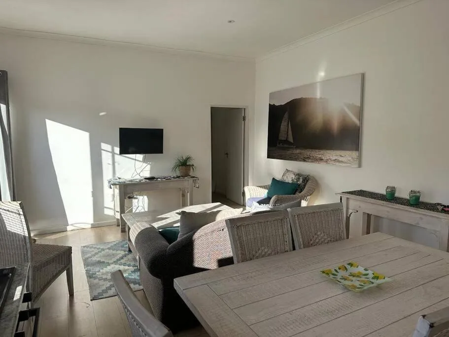 Second lounge corner with wall-mounted TV, sailboat artwork and wicker dining chairs