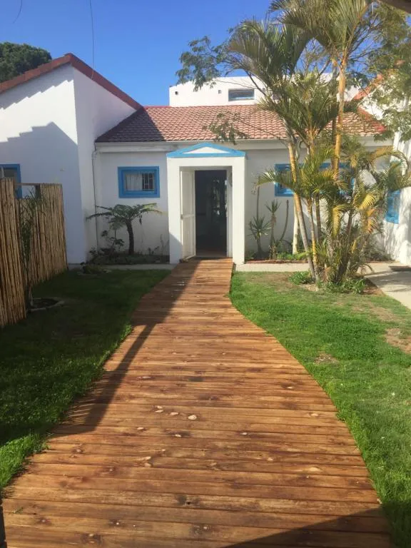 White cottage with blue-trimmed windows and a timber boardwalk winding through the garden