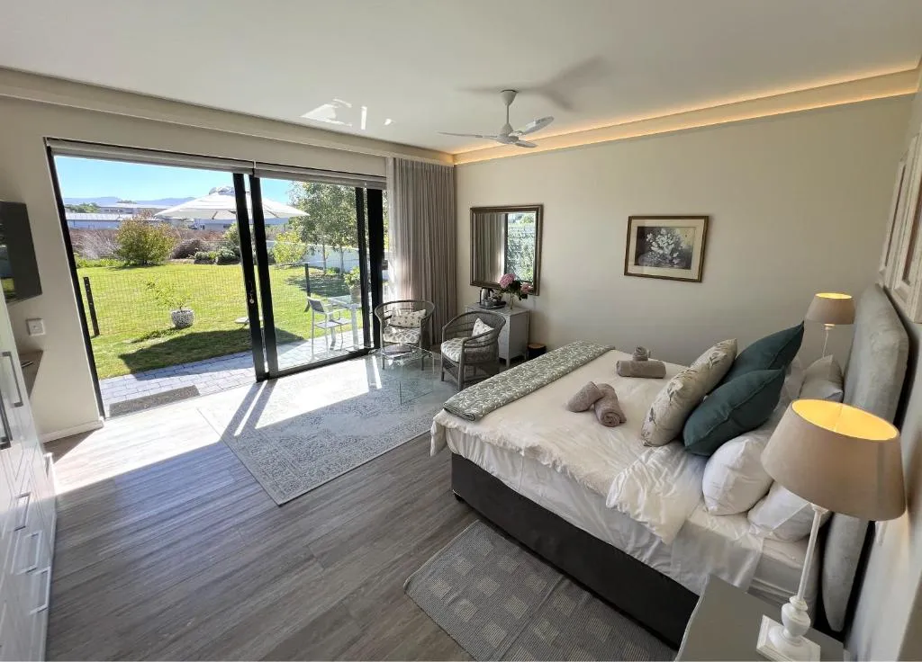 Bedroom with full-height glass doors opening onto a lawned garden with distant hills