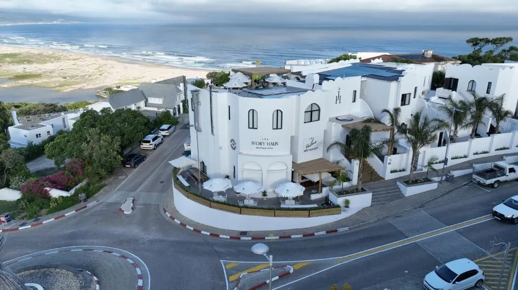 Aerial daytime view of the hotel's curved white facade across the road from the beach