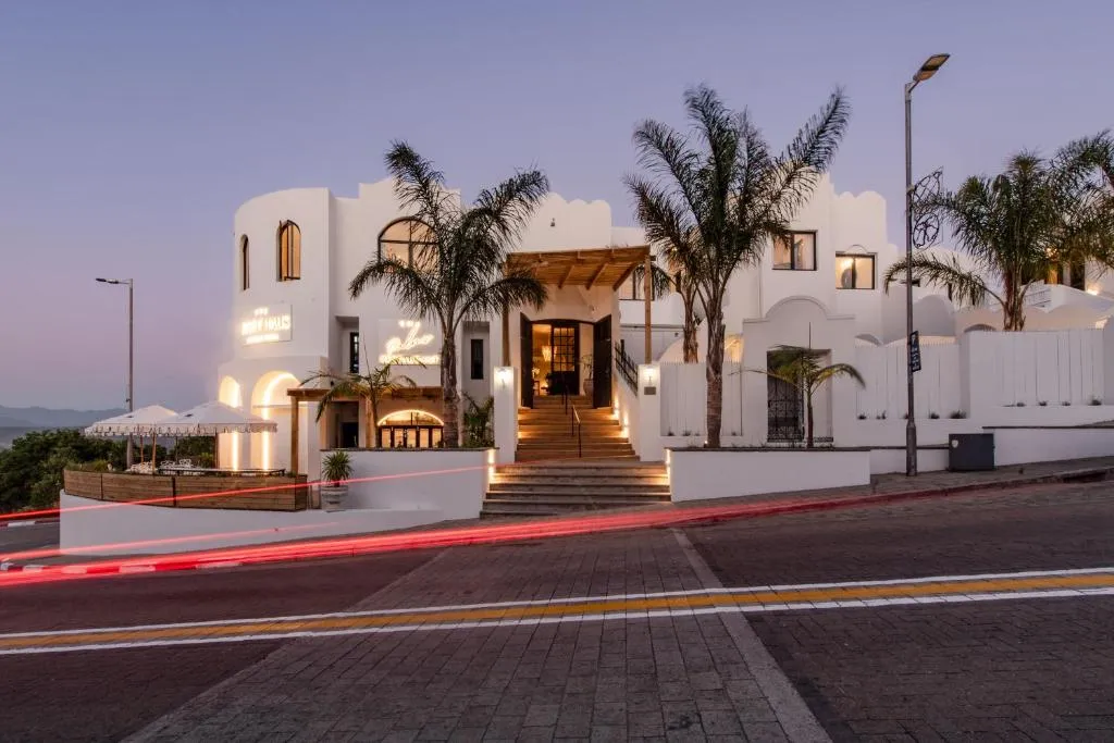 Whitewashed hotel entrance at dusk with a staircase up to arched doors flanked by palm trees