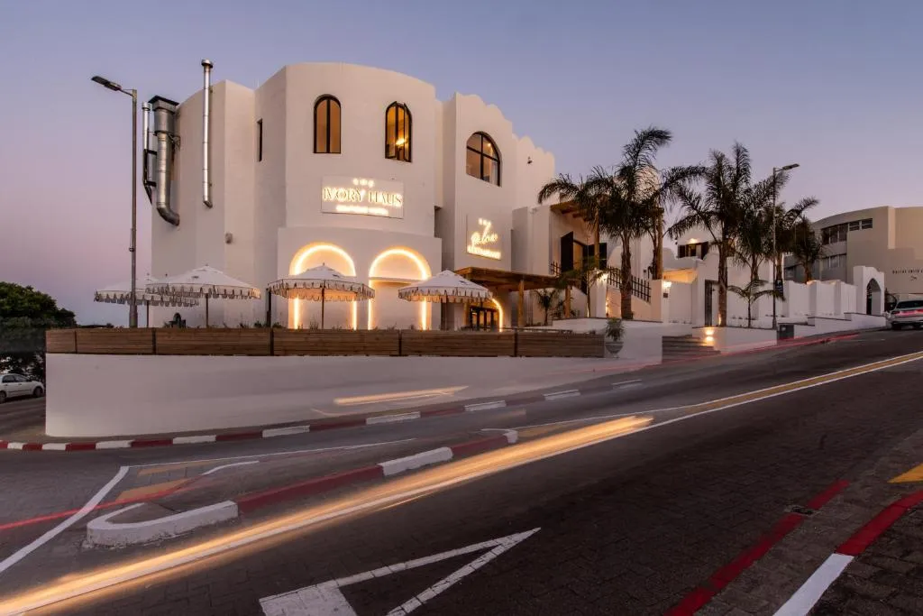 Ivory Haus boutique hotel lit up at dusk with arched windows, palm trees and outdoor umbrellas