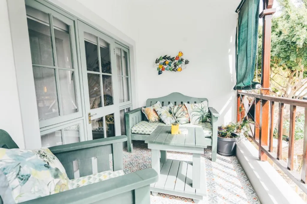 Balcony lounge with sage-green outdoor sofas on patterned tile, screened by surrounding trees