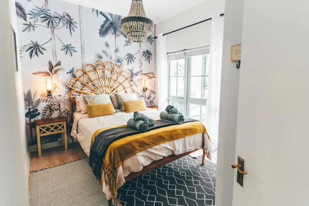 Bedroom with tropical leaf-print wallpaper, a rattan peacock headboard and a beaded pendant light