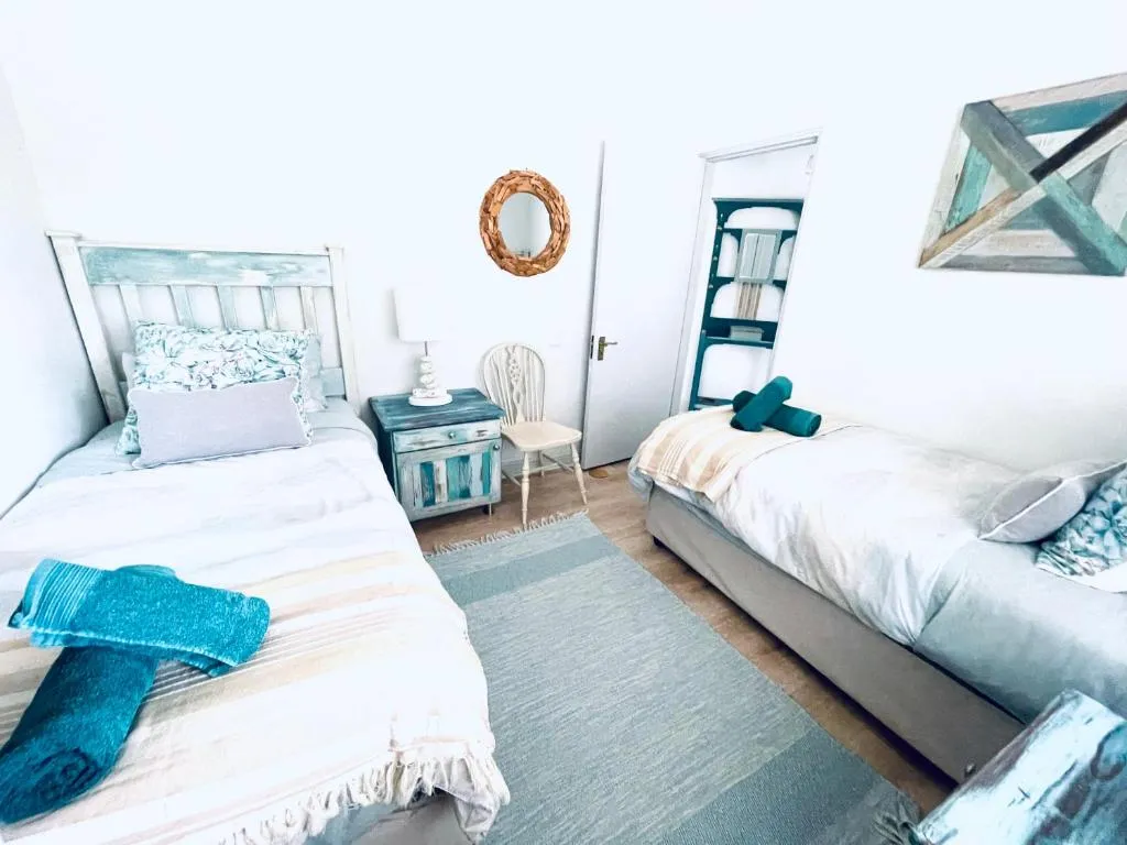 Twin bedroom in weathered teal and white with a driftwood-framed mirror and rolled towels