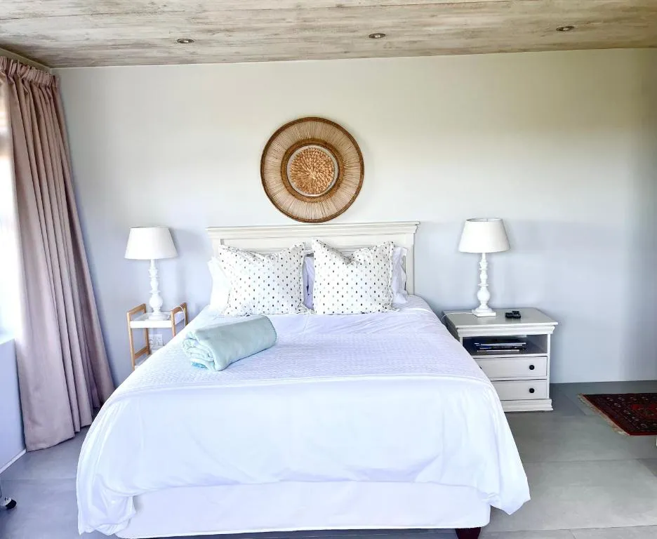 Bed with a white panelled headboard and a round woven wall disc above the pillows