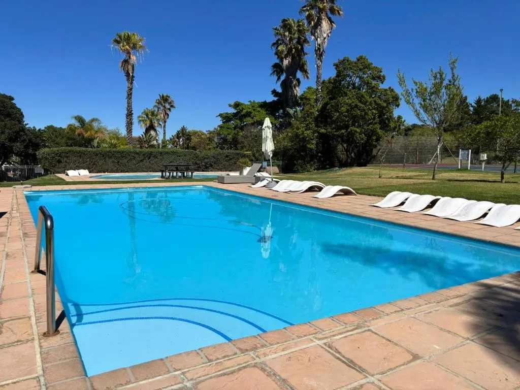 Shared estate pool with loungers, palm trees and a tennis court beyond the hedge