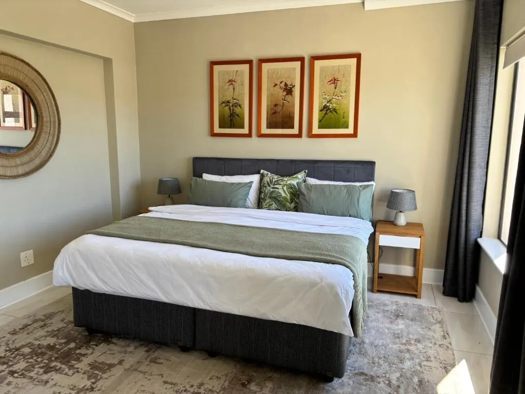 Main bedroom with a charcoal upholstered headboard and a round rattan mirror