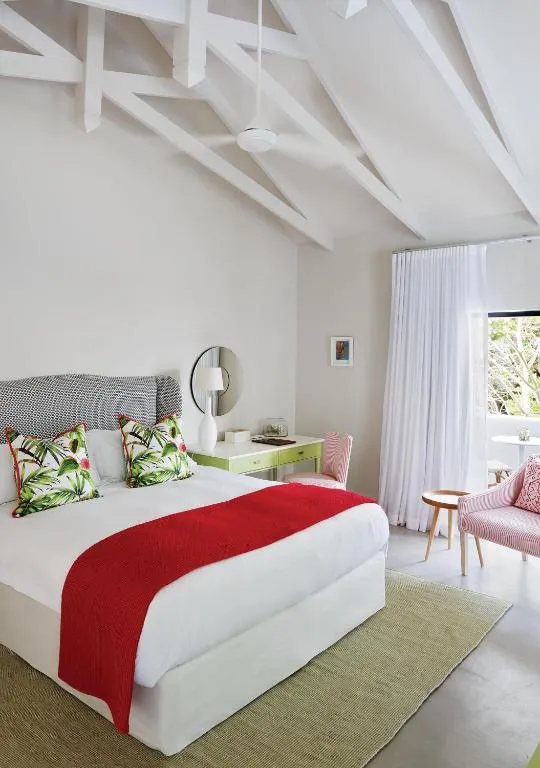 Bedroom with exposed white roof trusses, a grey headboard and a red throw