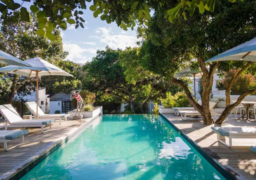 Tree-shaded pool deck with striped umbrellas, loungers and a poolside bronze statue
