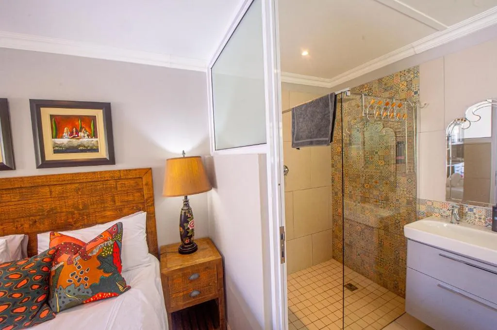 Bedroom with colourful cushions beside an open doorway into a tiled walk-in shower