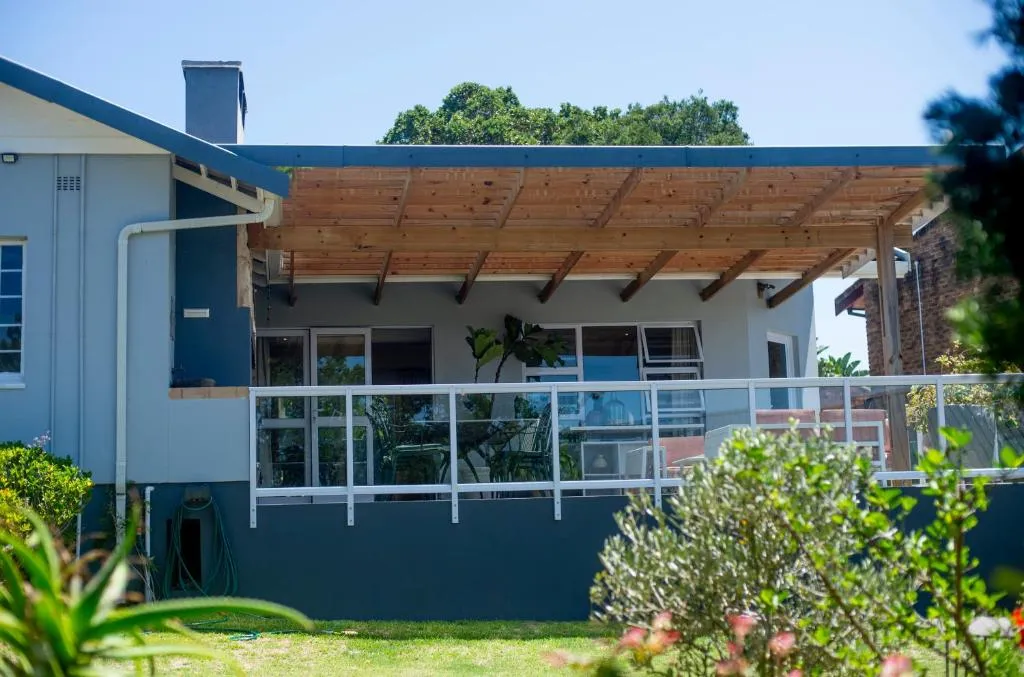 Coastal home exterior with a timber-beamed pergola patio and glass balustrade opening onto the garden