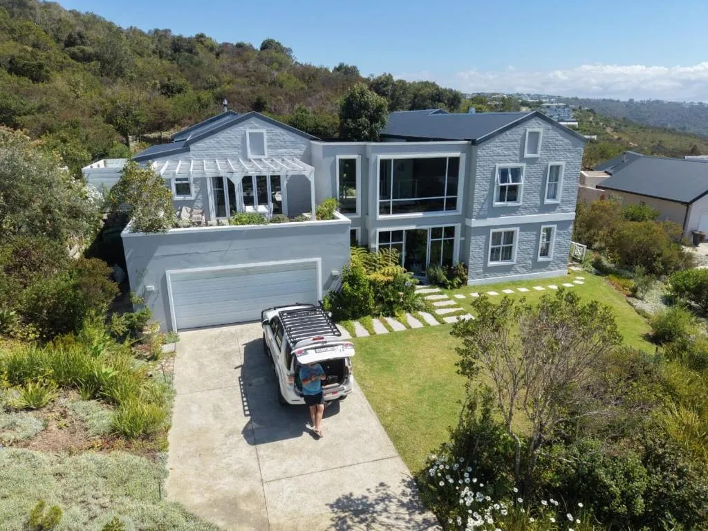 Aerial view of the house and garden on a wooded hillside, with a car parked in the driveway