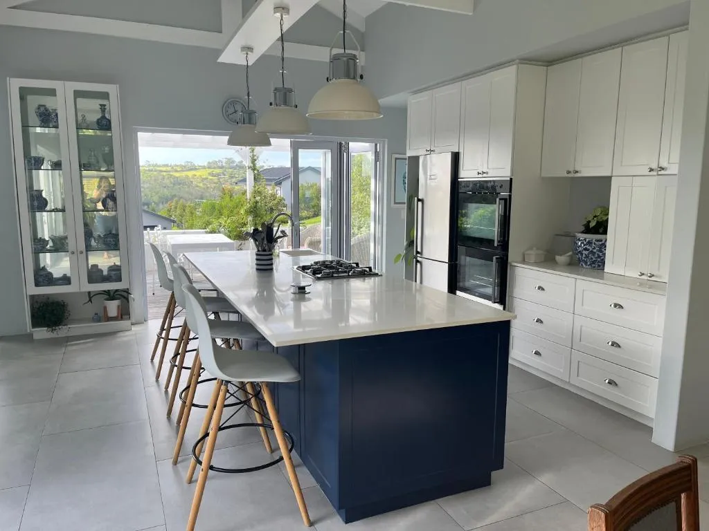 Kitchen with a navy island, bar stools and white cabinetry opening onto the garden terrace