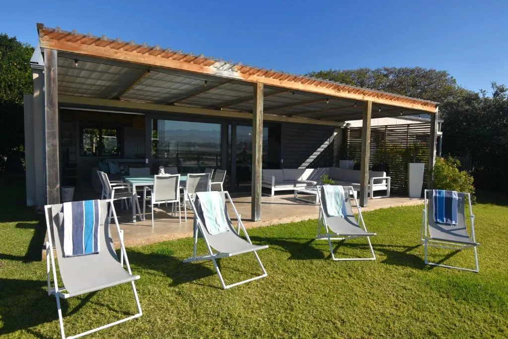 Covered wooden deck with a dining table and lounge seating, opening onto the garden lawn