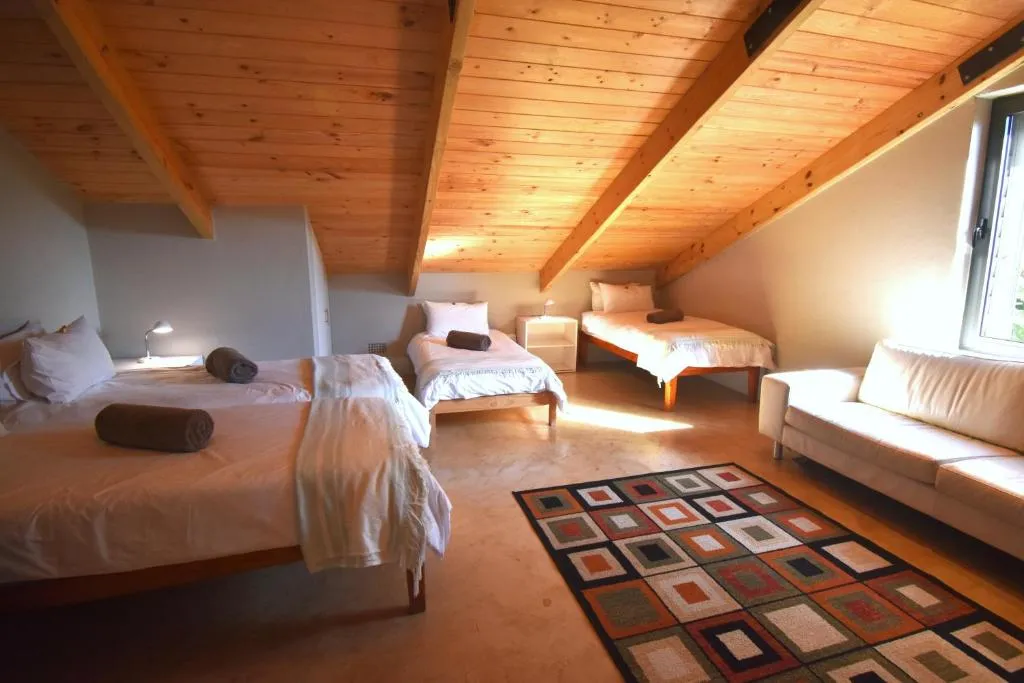 Loft bedroom under a pitched wooden-beamed ceiling with three single beds and a reading sofa