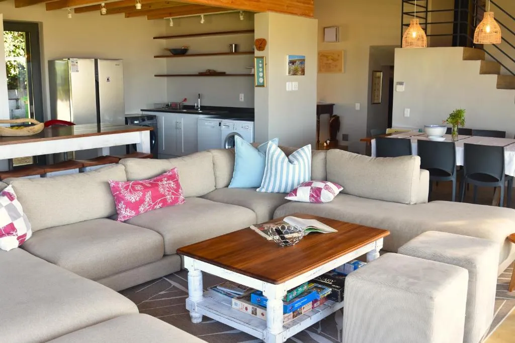 Open-plan lounge with a corner sofa, in view of the kitchen with fridge, sink and washing machine