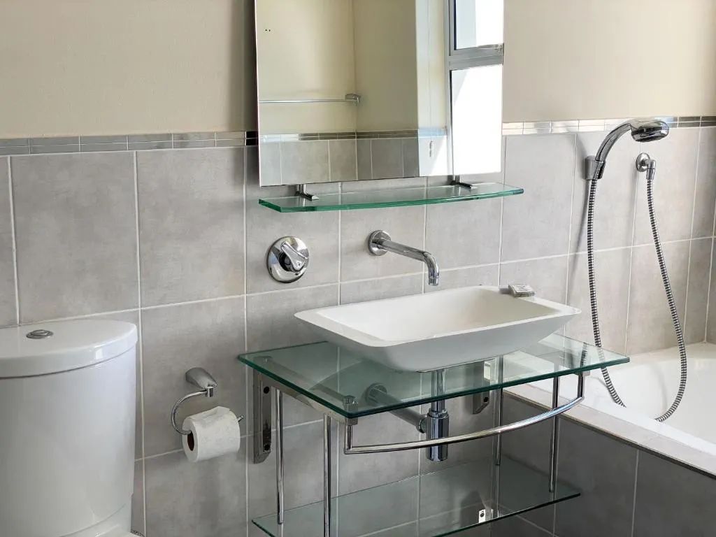 Bathroom with a rectangular vessel basin on a glass shelf, wall-mounted tap and bathtub