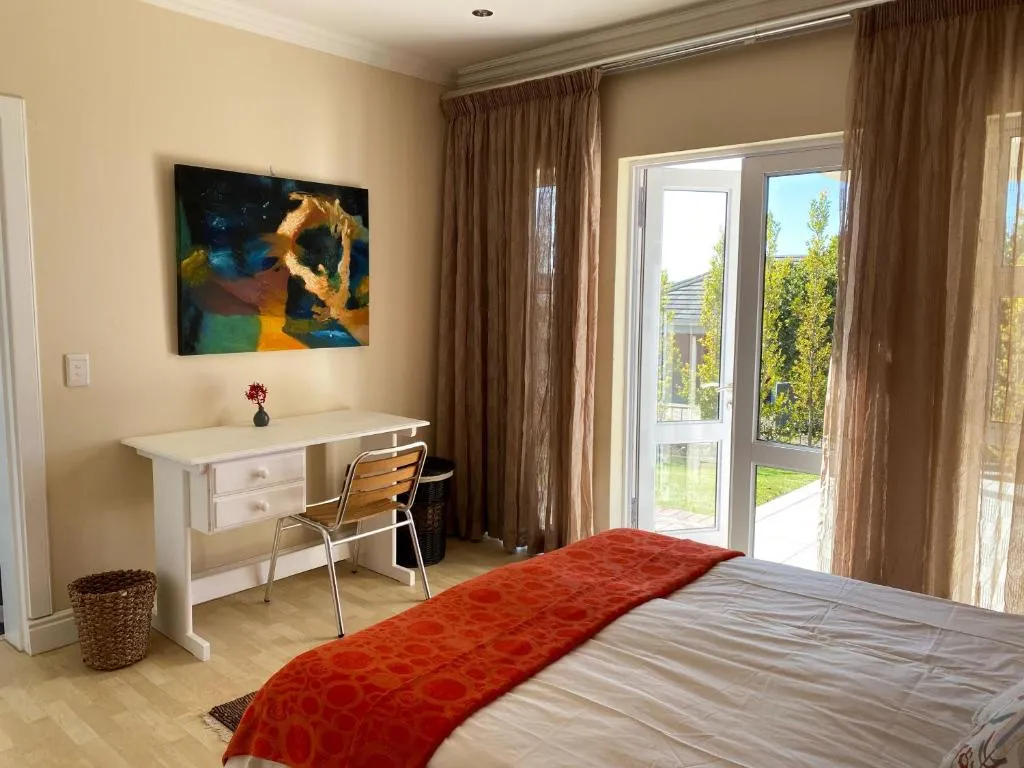Bedroom with an orange throw, sheer curtains and glass doors opening directly onto the garden patio