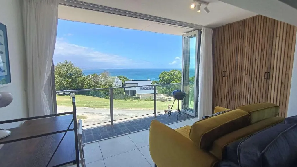 Living area opening onto a timber-walled balcony with a braai and sea view beyond