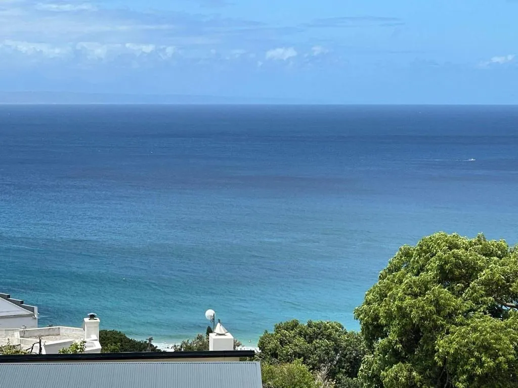 Elevated sea view over neighbouring rooftops and treetops, with distant mountains on the horizon