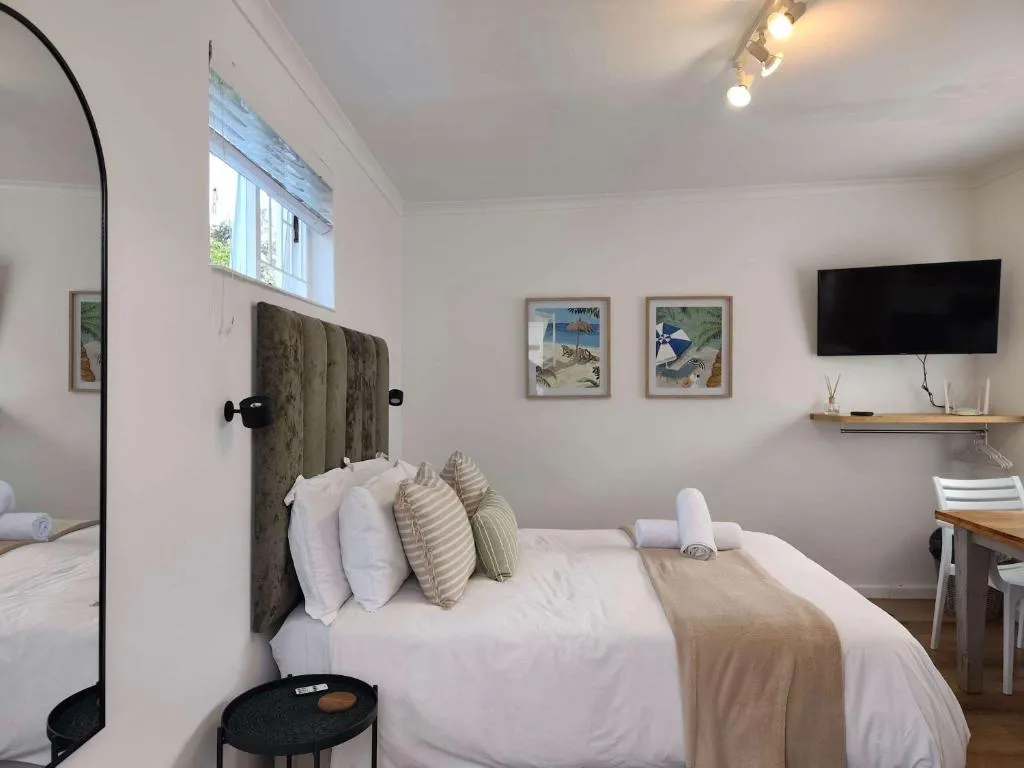 Bedroom with a plush green headboard, wall-mounted TV and framed beach-themed prints