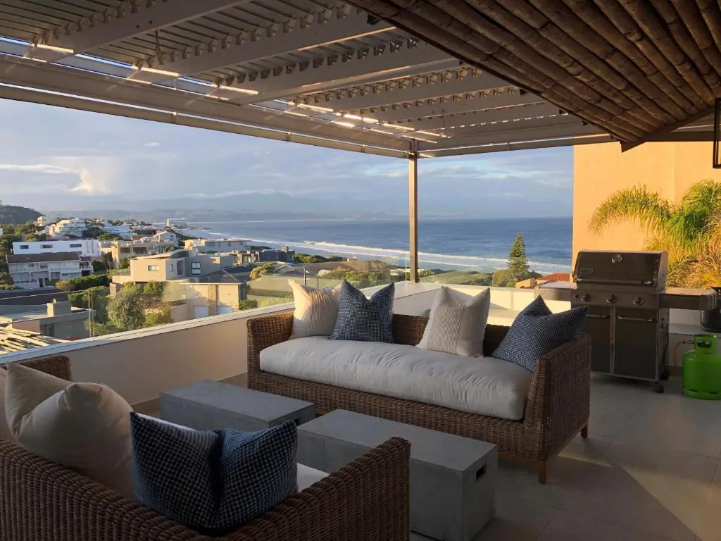 Rooftop terrace with wicker lounge seating, a gas braai and a wide view over rooftops to the sea