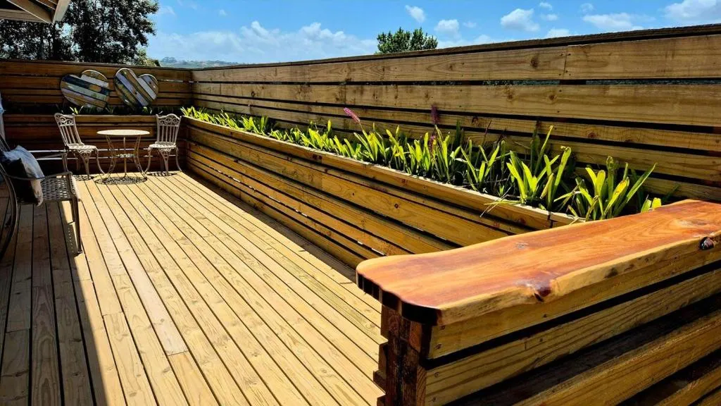 Private wooden deck with a white bistro table, chairs and a planted greenery border