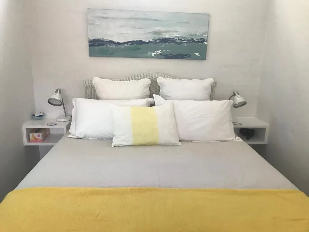 Bedroom with a cane headboard, ocean-wave artwork above the bed and a yellow throw