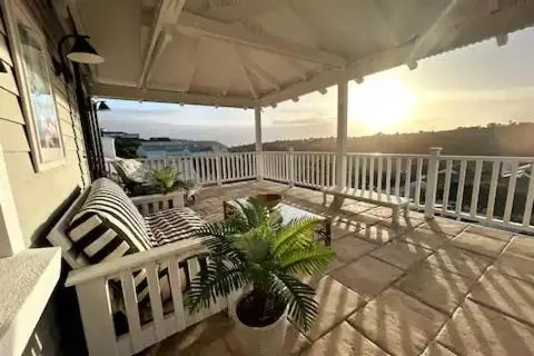 Covered terrace with white balustrades overlooking the hillside towards a distant sea view