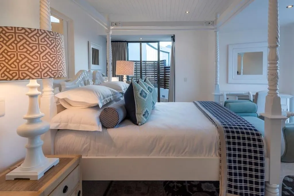 White four-poster bed with navy check throw, sliding door onto the terrace beyond