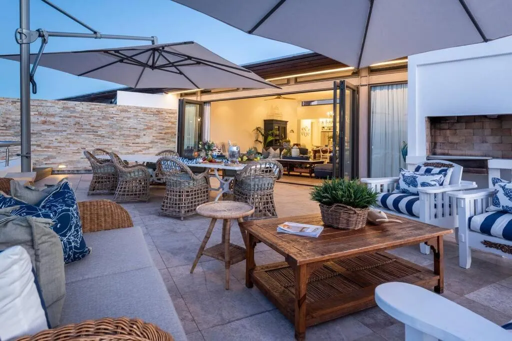 Rooftop terrace lounge at dusk with wicker chairs, a built-in braai and umbrellas beside the open living room