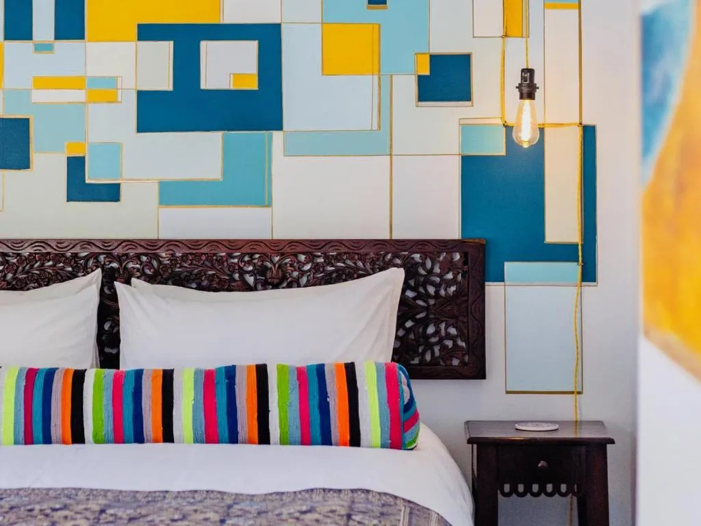 Carved wooden headboard against a colourful geometric mural above the bed