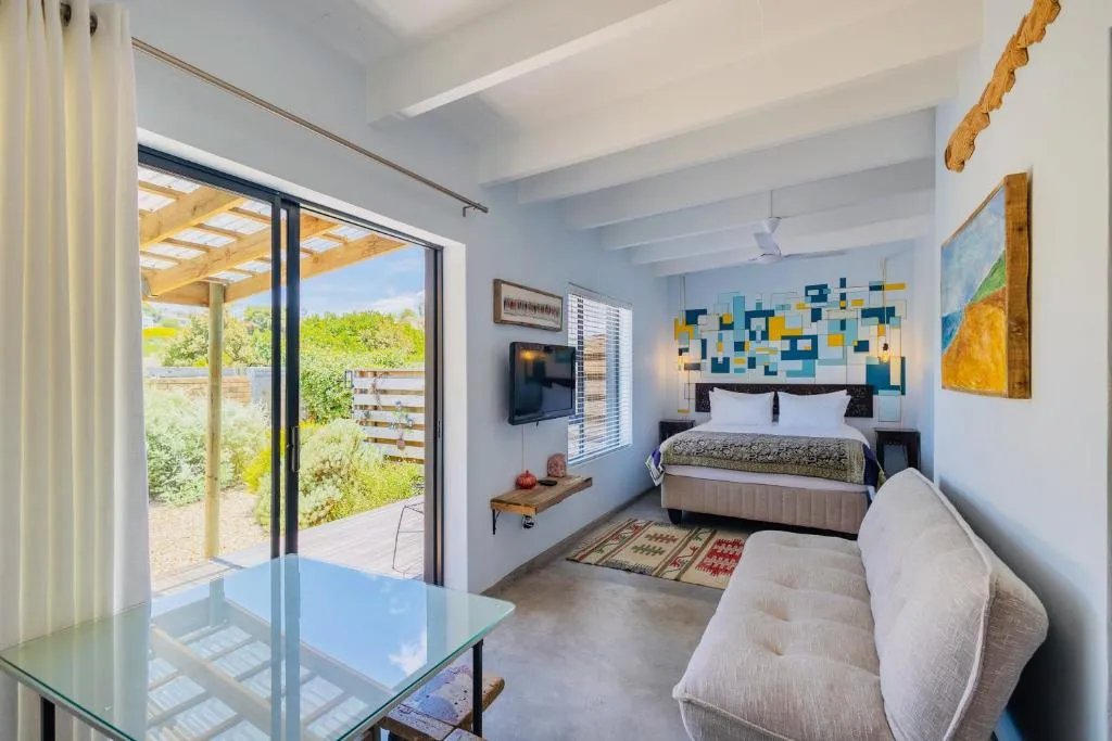 Open-plan studio with a bed, sofa and sliding doors onto a covered timber deck