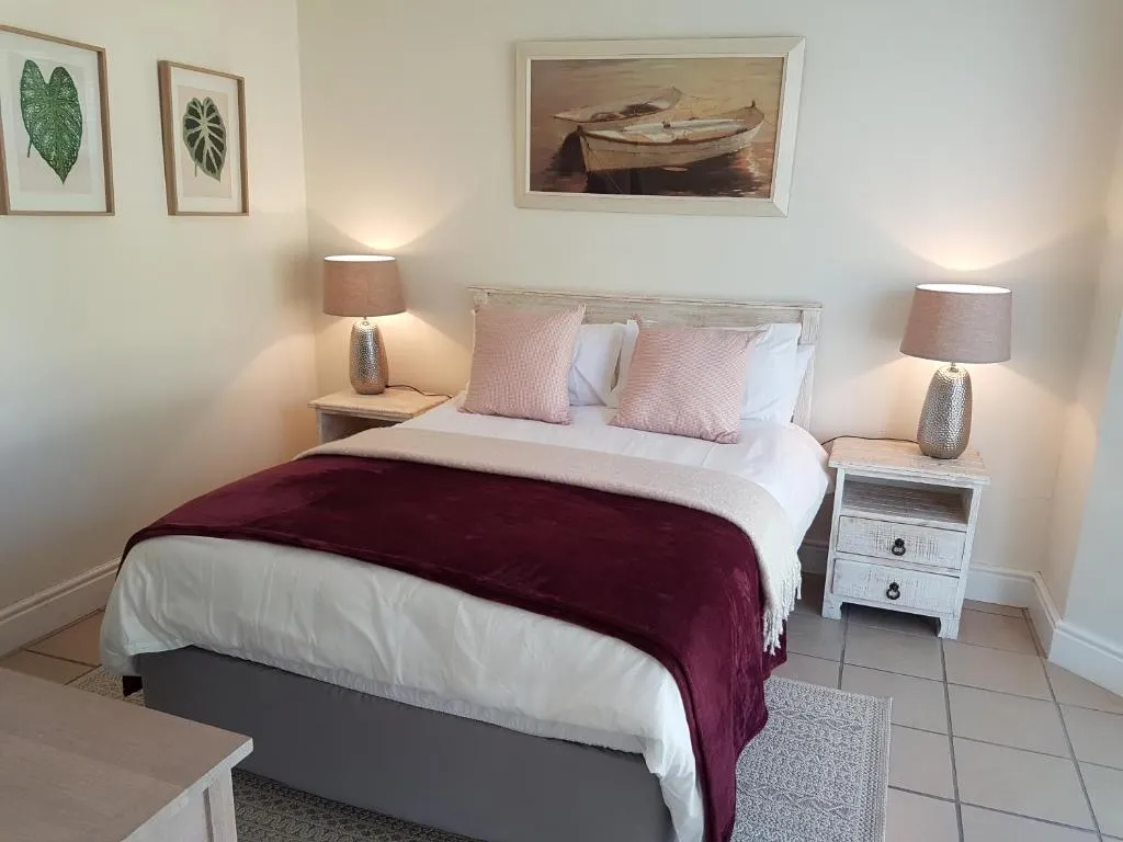 Main bedroom with a burgundy throw, boat artwork above the headboard and bedside lamps