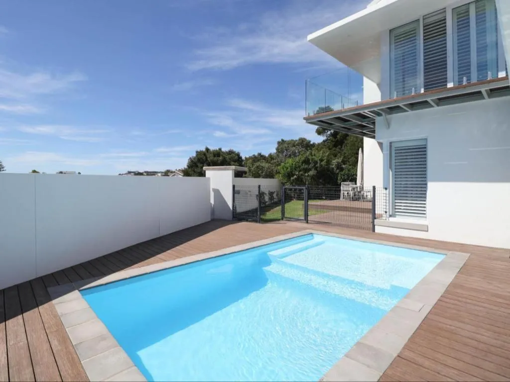 Rectangular pool on a timber deck bordered by a tall white boundary wall