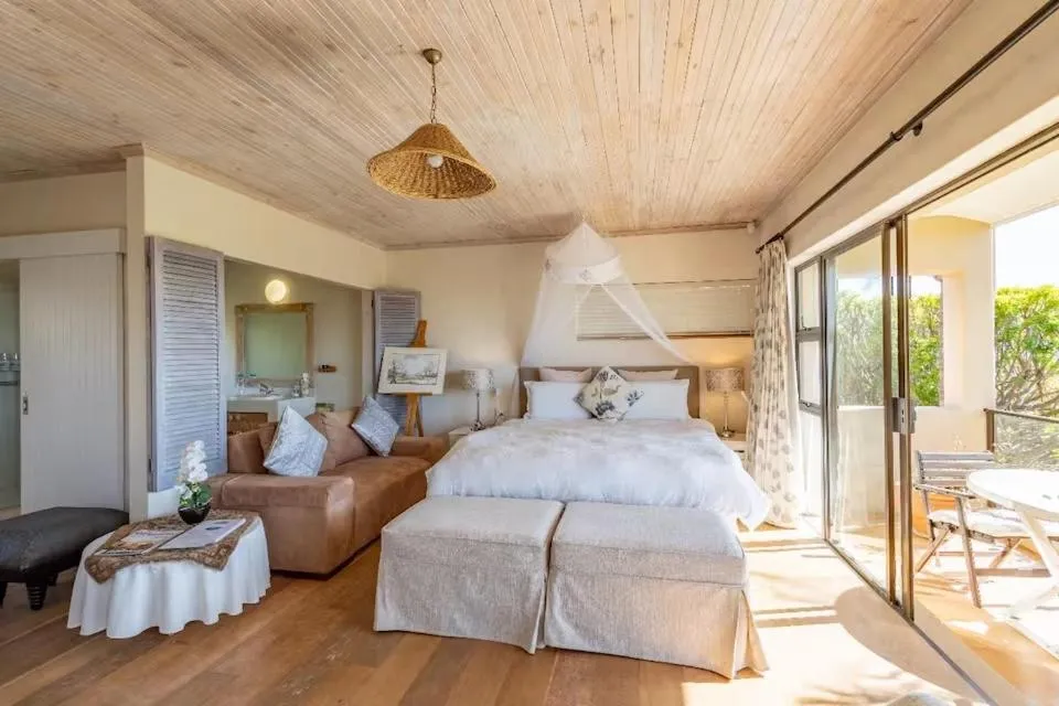 Studio bedroom with a mosquito-net canopy, tan leather couch and sliding doors to a private balcony