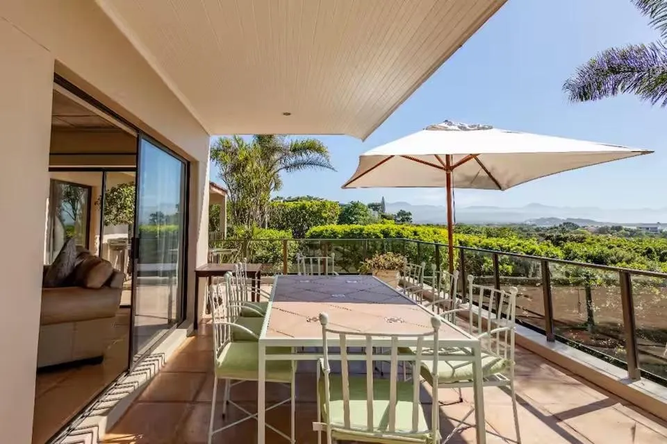 Covered terrace with a long dining table, umbrella and a view over treetops to distant mountains