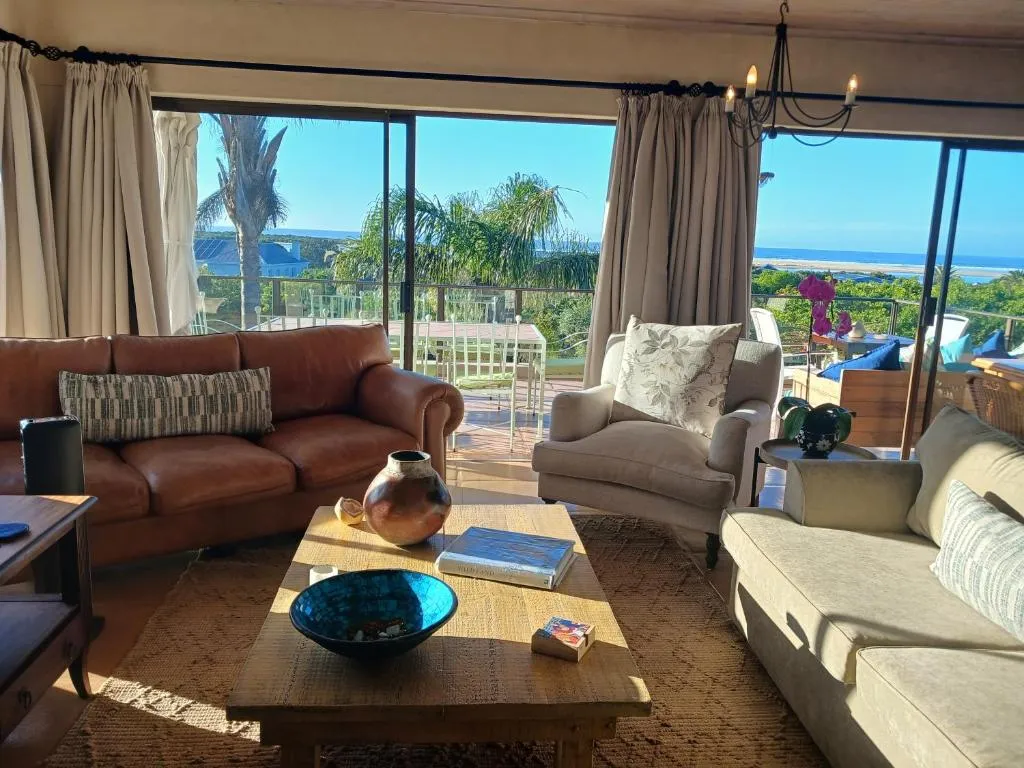 Lounge with leather and cream sofas opens onto a balcony with palm trees and a strip of ocean beyond