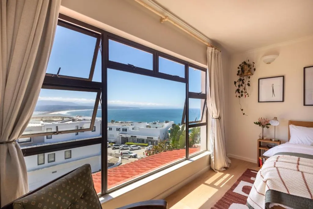 Bedroom with floor-to-ceiling windows opening onto a wide sea and coastline view