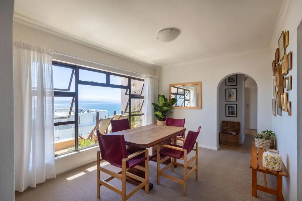 Dining room with a wooden table for six and floor-to-ceiling windows over the sea