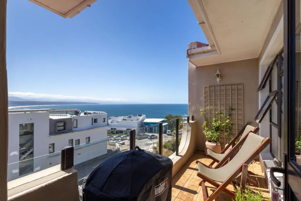Balcony terrace with deck chairs, a covered braai and an open sea view over rooftops